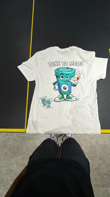 The white Take Ya Meds tee laid flat, showing the large mascot back graphic